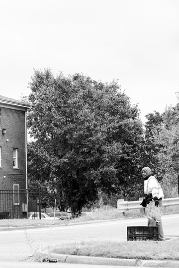 Mr. John stands next to a crate outside near a street.