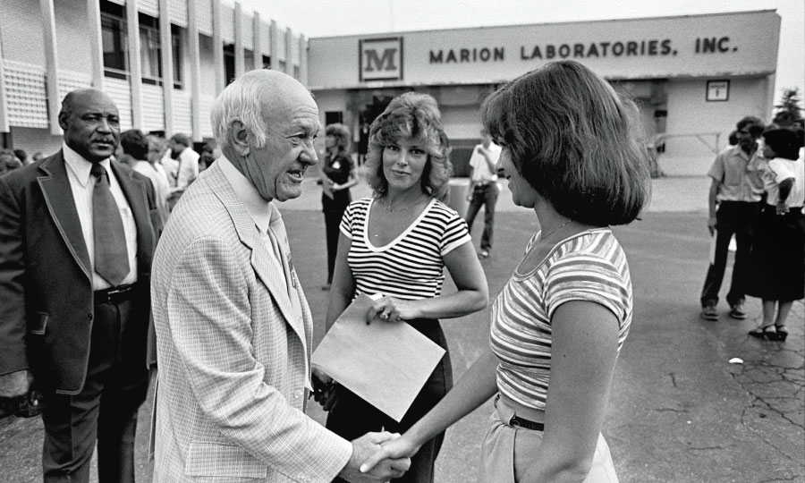 Ewing Kauffman shakes hands with a woman outside of Marion Laboratories, Inc.