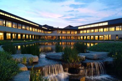 The arms of the Kauffman Foundation building reach east towards Troost Ave. A pond with two waterfalls is pictured behind the building.