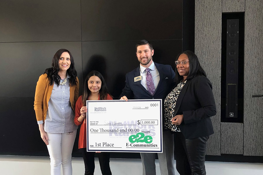A group of four hold a giant check from NetWork Kansas for $1000.00, the first prize winnings for NetWork Kansas E-Community Youth Entrepreneurship Challenge, 2019-2020.