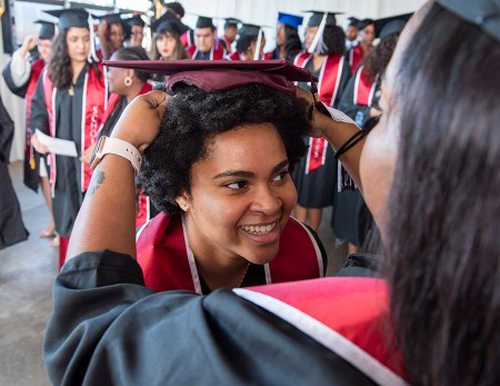 A moment from the KSI graduation ceremony in 2019. One graduate helps another with their graduation cap.