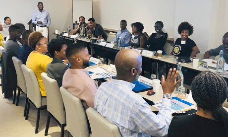 Nineteen people sit together in conversation at two long conference room tables at a Builders and Benefactors convening