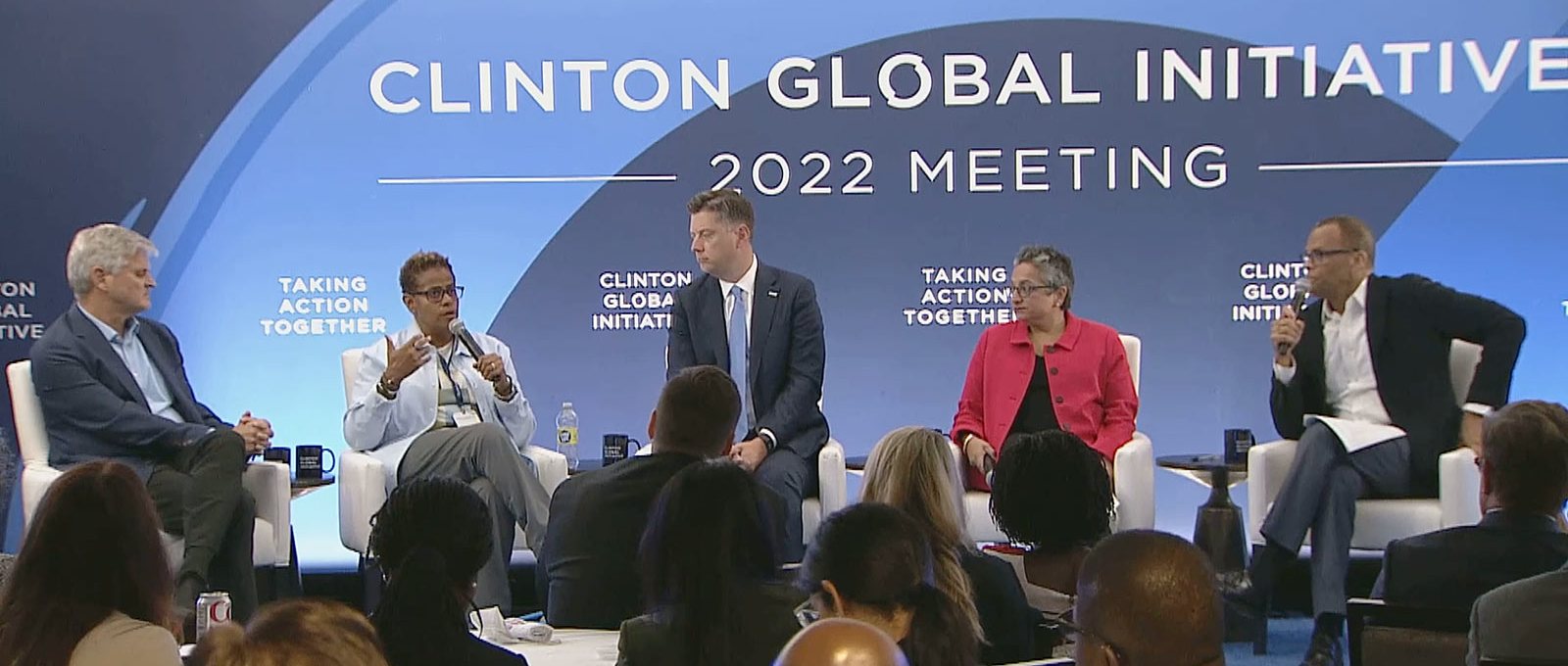 A panel of five entrepreneurship leaders sit on a stage in front of a live audience answering questions. Behind them is a screen that reads "Clinton Global Initiative, 2022 Meeting"