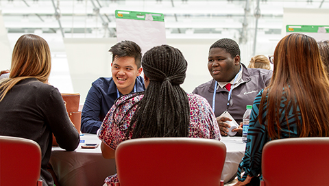 A group of students sit around a table at a learning conference.