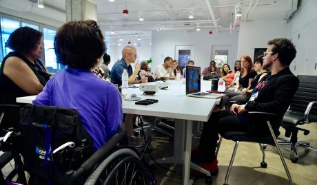 A cohort of sixteen entrepreneurs with disabilities part of the 2Gether-International accelerator program sit around a long table inside a coworking space.