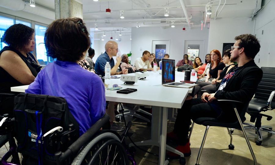 A cohort of sixteen entrepreneurs with disabilities part of the 2Gether-International accelerator program sit around a long table inside a coworking space.