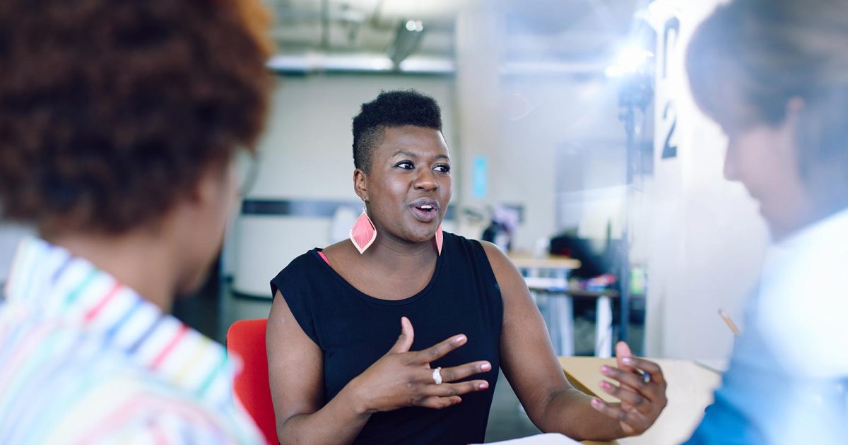 A Black entrepreneur wearing pink teardrop earrings talks with their hands.