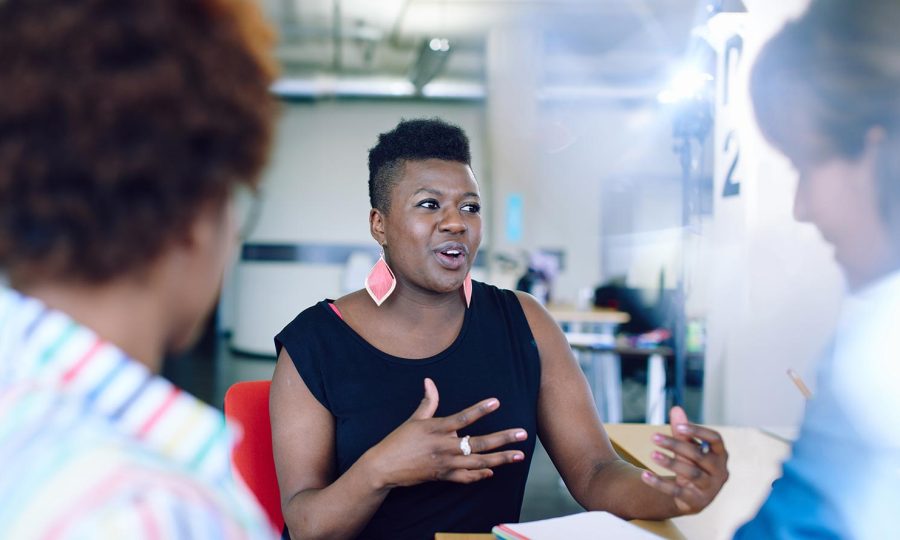 A Black entrepreneur wearing pink teardrop earrings talks with their hands.