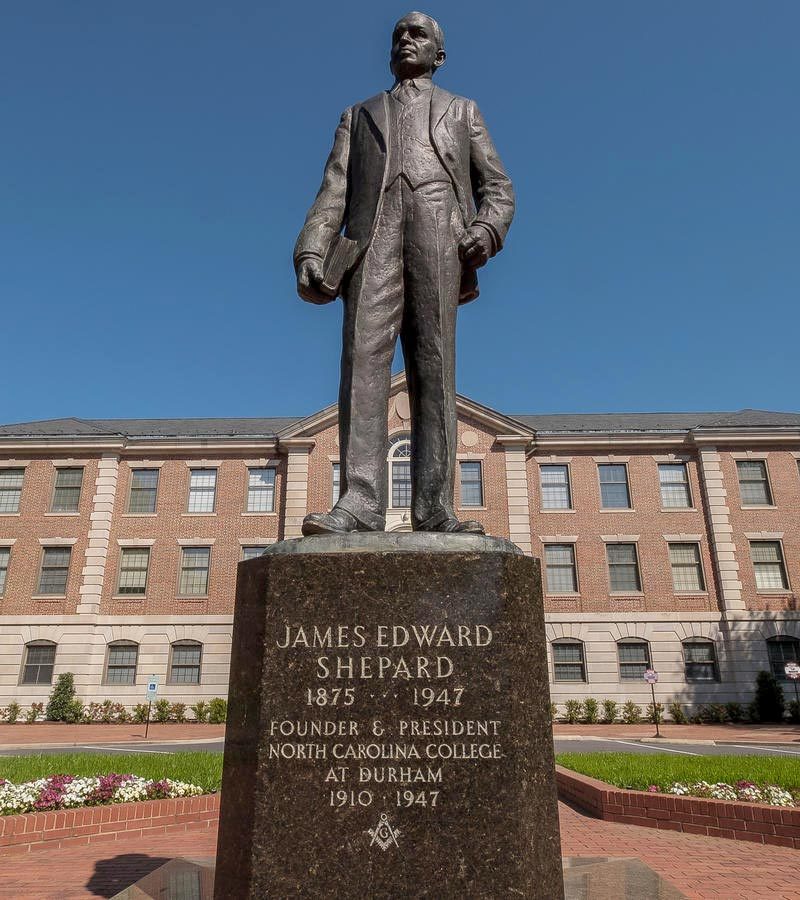 A statue of a man in front of a brick college building with an inscription that reads: "James Edward Shepard 1875-1947, Founder & President, North Carolina College at Durham 1910-1947"