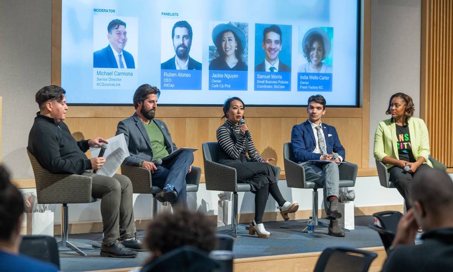 Kansas City entrepreneurs sit on a panel on stage in front of a live audience. From left to right: Michael Carmona, Ruben Alonso, Jackie Nguyen, Samuel Morris, and India Wells-Carter.