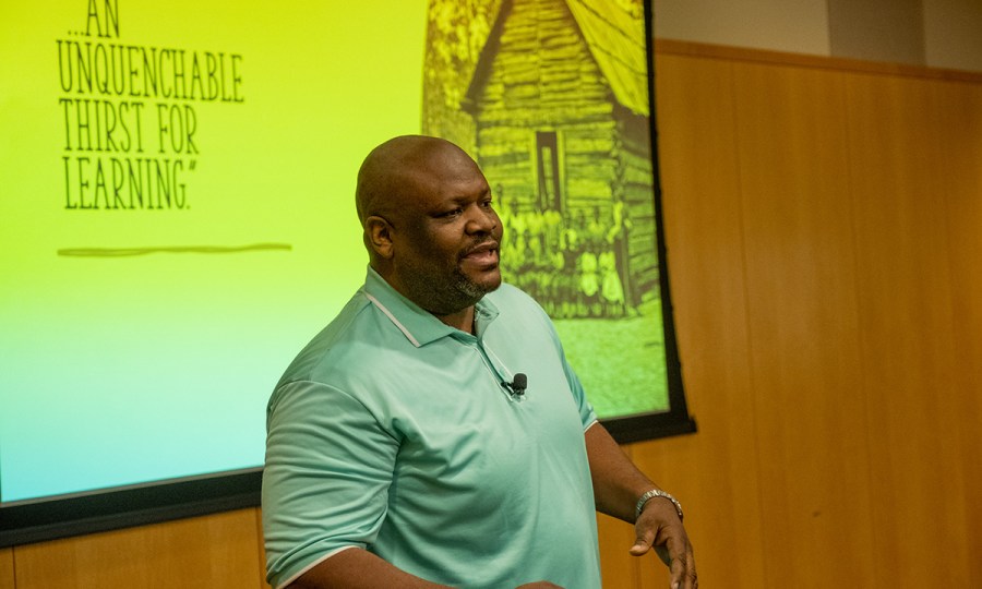 Spark Bookhart speaks at the Amplify 2022 conference in Kansas City, Missouri. Behind him is a quote projected onto the wall: "...An unquenchable thirst for learning."