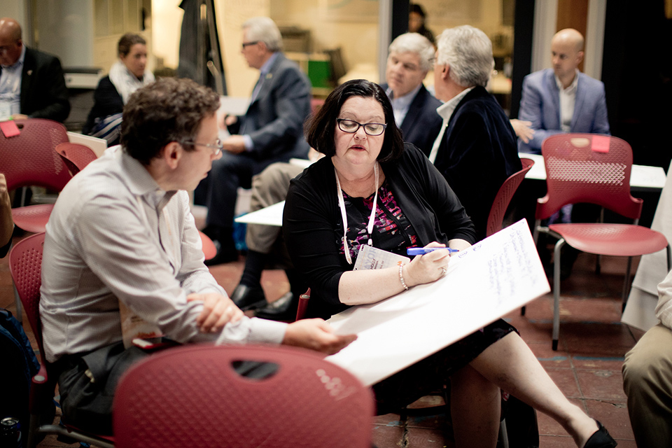 Two attendees at the Mayors Conference on Entrepreneurship talk and write notes on a poster.