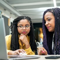 Two young people sit in front of a shared laptop.