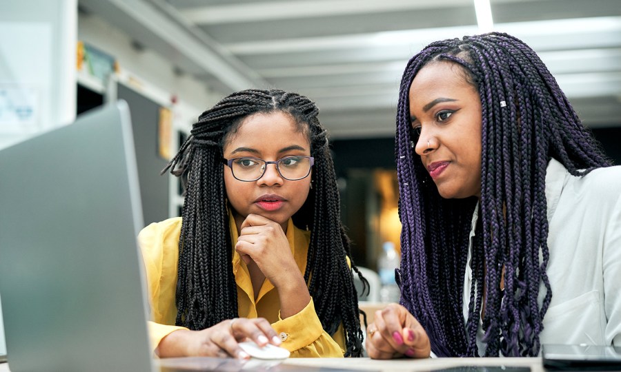 Two young people sit in front of a shared laptop.