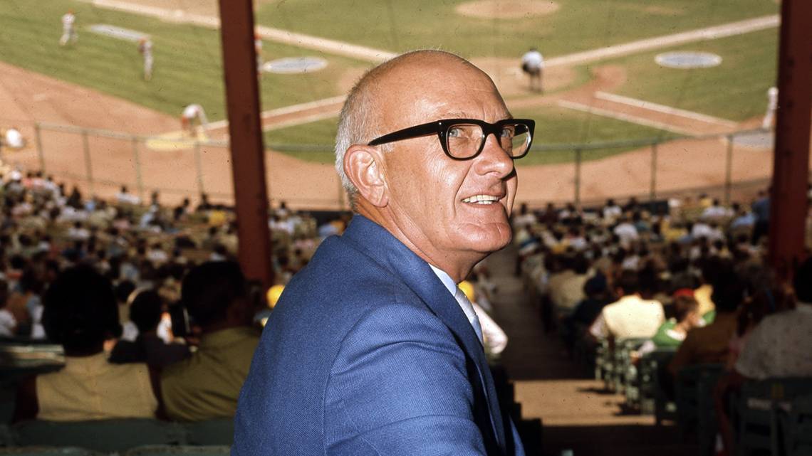 Ewing Marion Kauffman, wearing thick-rimmed glasses and his classic blue suit, attends a baseball game.