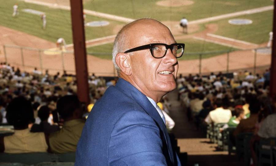 Ewing Marion Kauffman, wearing thick-rimmed glasses and his classic blue suit, attends a baseball game.