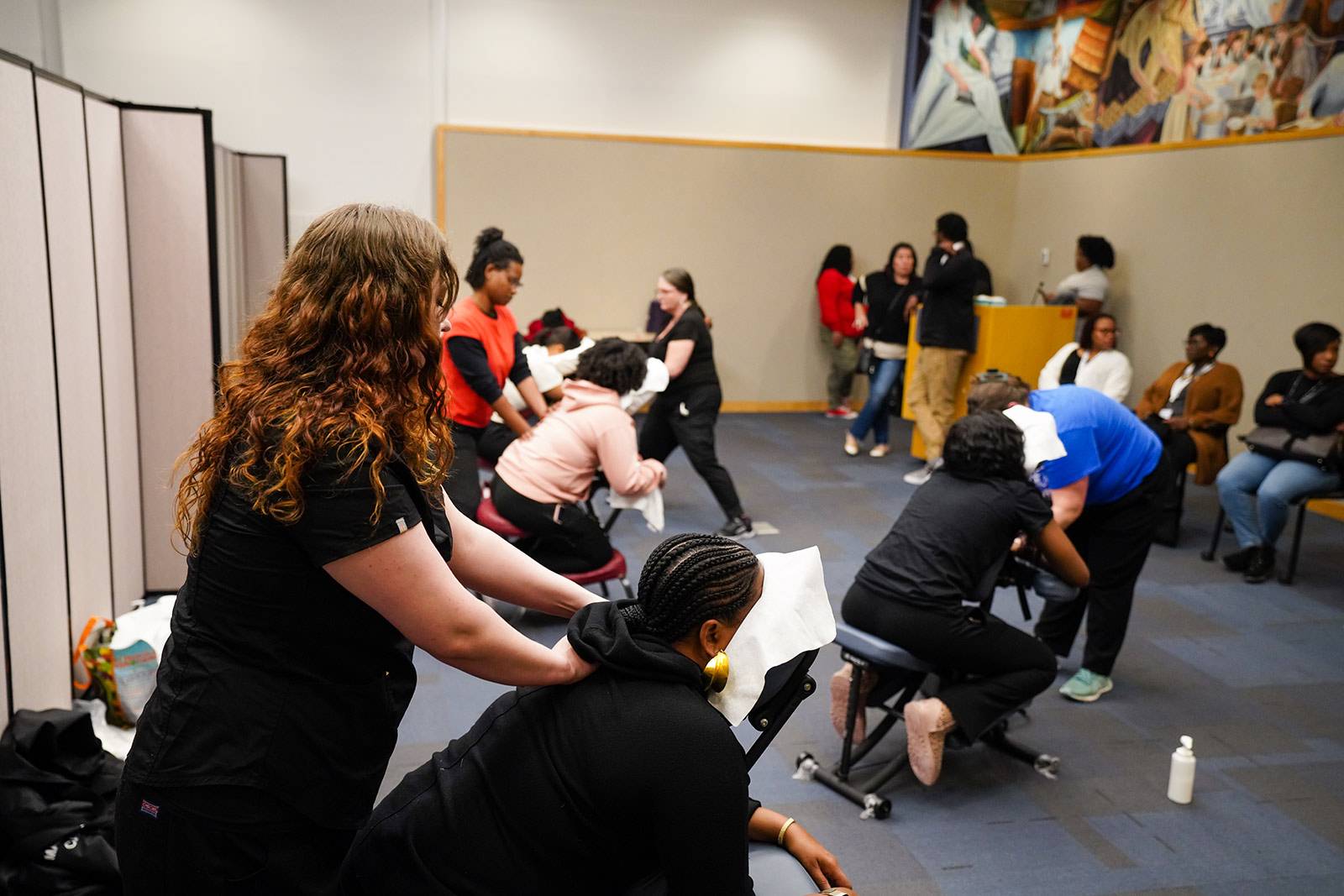 Three people receive massages with more people waiting their turn around the room.