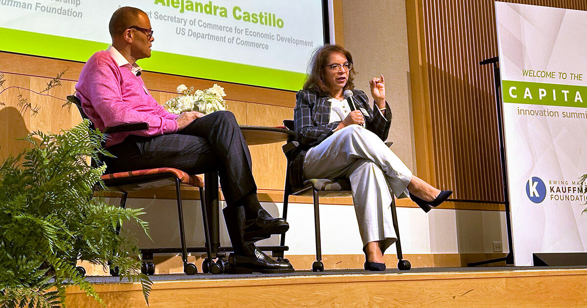 Alejandra Y. Castillo, Assistant Secretary of Commerce for Economic Development with the U.S. Department of Commerce, speaks into a microphone on stage at the Capital Innovation Summit. Philip Gaskin, vice president of Entrepreneurship with the Ewing Marion Kauffman Foundation, sits beside her on stage.