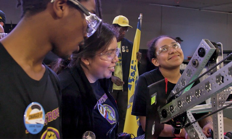 Three students wear safety goggles behind a laptop computer that controls the robot they built for the FIRST Robotics spring competition, 2023.