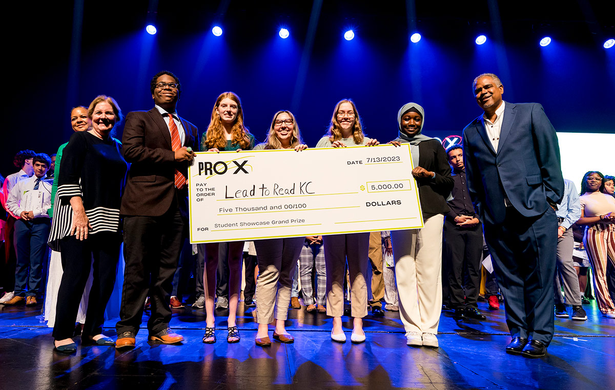 ProX students stand on a stage holding an oversized check made out to Lead to Read for $5,000 grand prize.