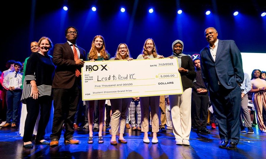 ProX students stand on a stage holding an oversized check made out to Lead to Read for $5,000 grand prize.