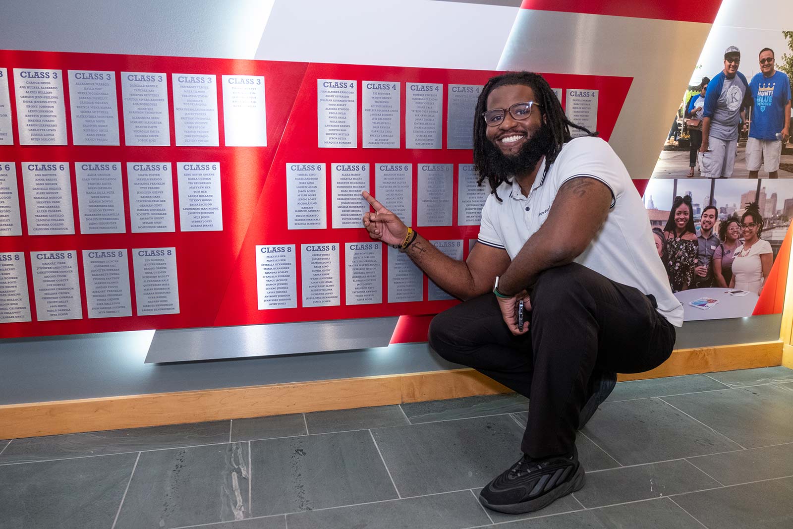 A KSI alum poses in front of the KSI Legacy Wall next to their name.