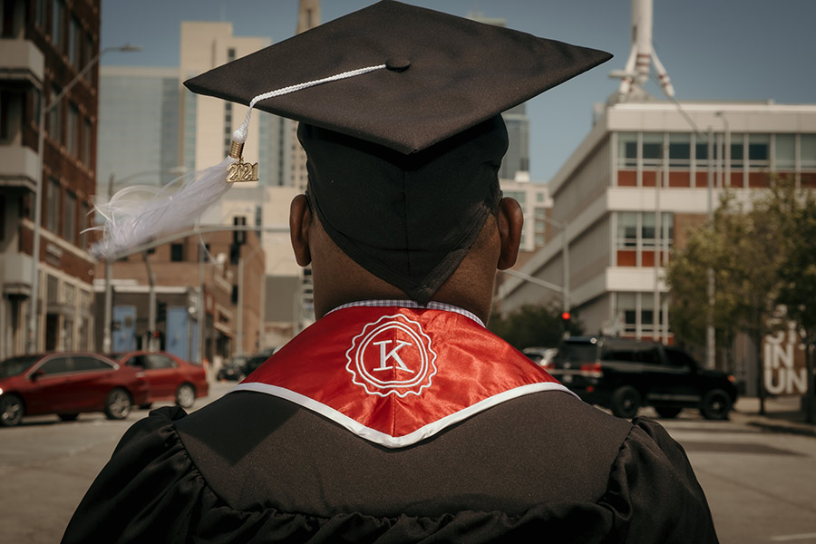A 2021 graduate looks down a Kansas City street wearing a graduation cap and Kauffman Scholars stole