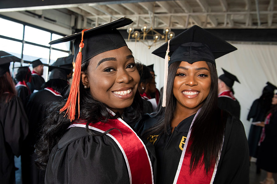 Two KSI graduates pose for a photo wearing caps, gowns, and Kauffman Scholars stoles.