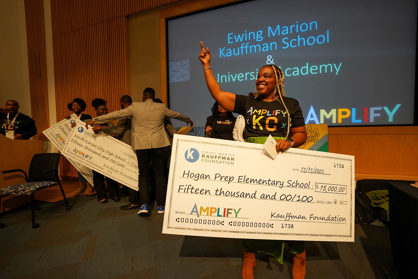 Amplify KC attendee and educator holds a life-sized check made out to Hogan Prep Elementary School for $15,000 from the Kauffman Foundation.