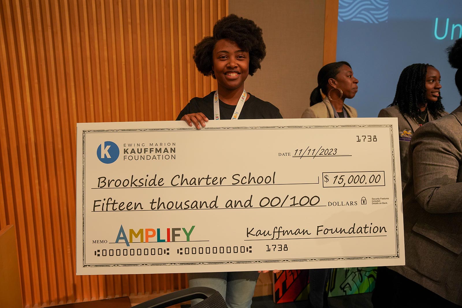 Monique Young holds a life-sized check made out to Brookside Charter School for $15,000 from the Kauffman Foundation during the Amplify conference