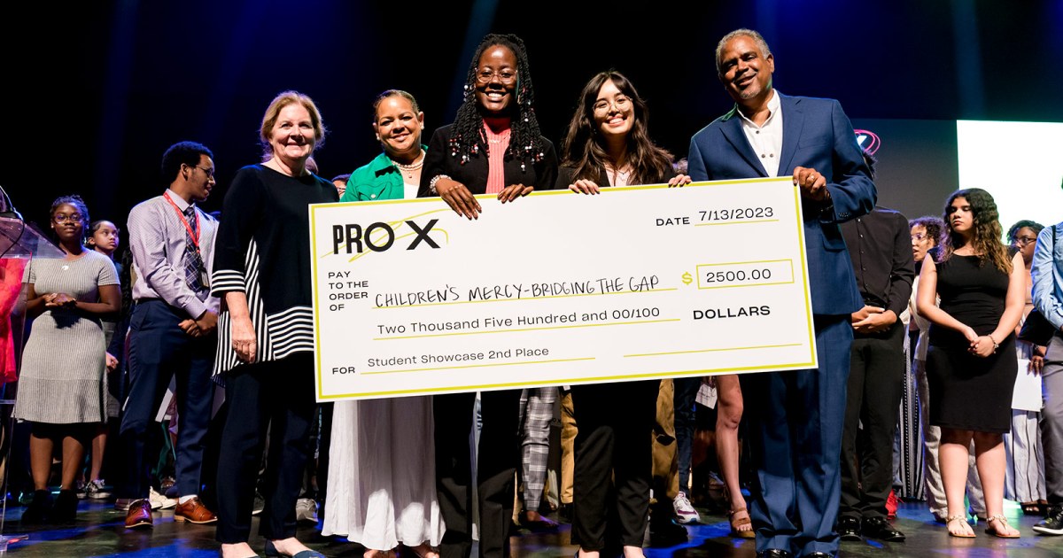 ProX students stand on stage holding a life-sized check made out to Children's Mercy – Bridging the Gap for $2500.