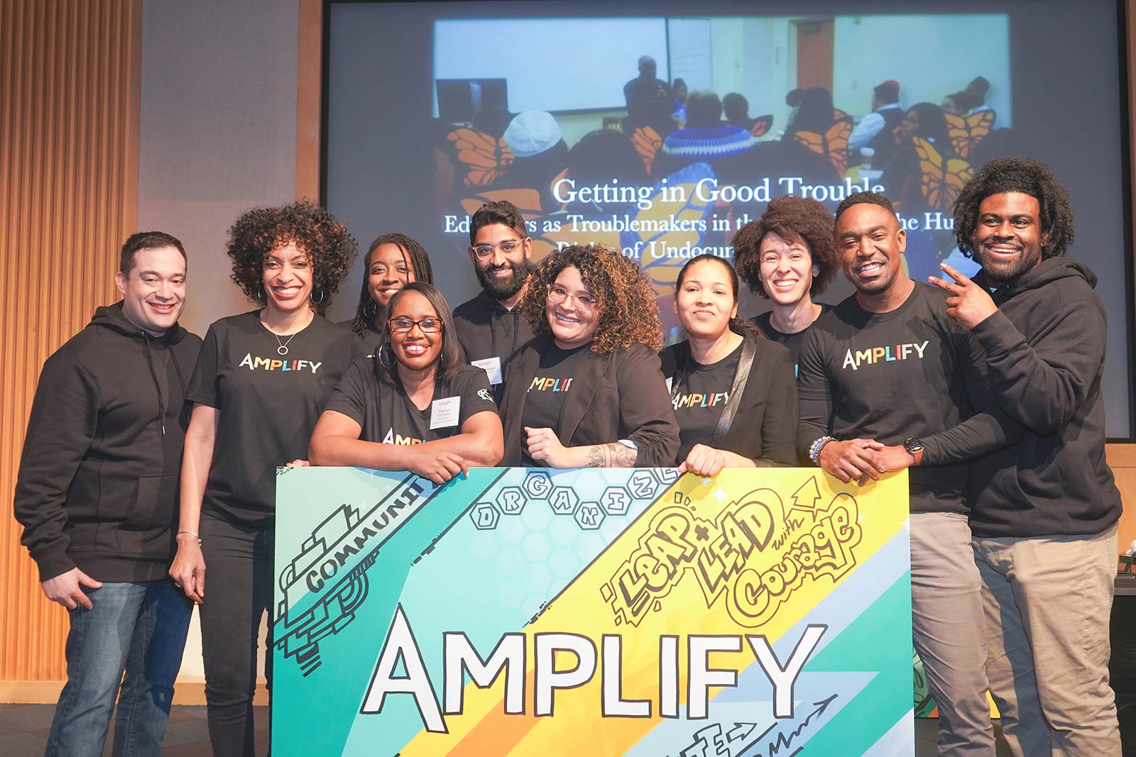 Amplify attendees pose for photo behind Amplify sign