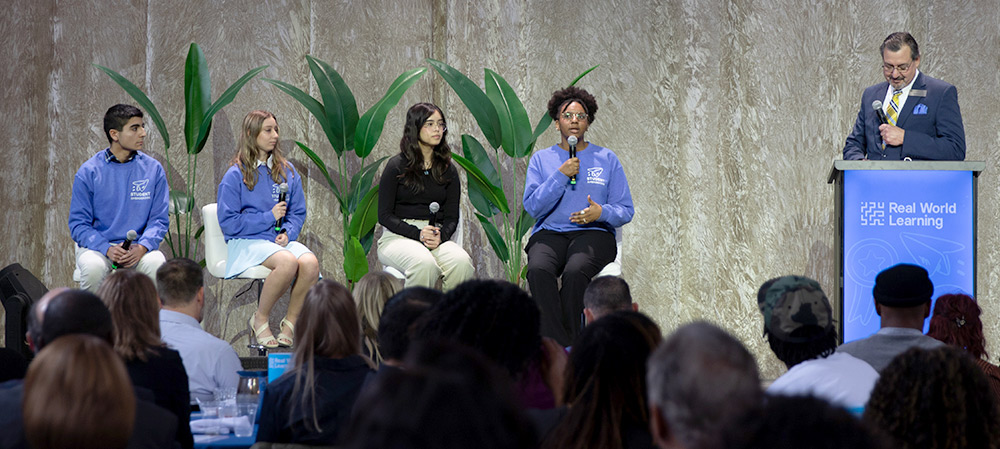 Students sit on a panel onstage with a facilitator