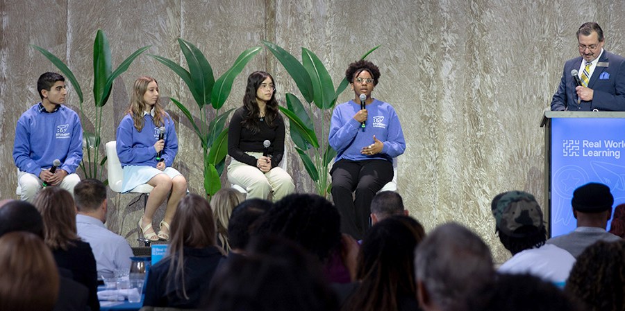 Students sit on a panel onstage with a facilitator