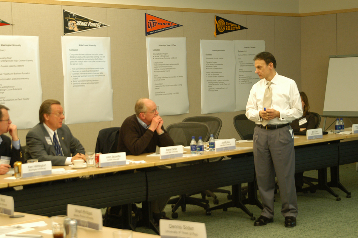 People sit around a table with college flags on the wall for Kauffman Campuses.