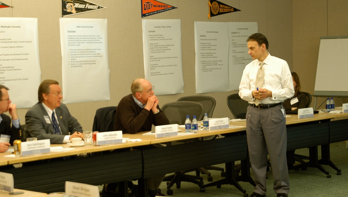 People sit around a table with college flags on the wall for Kauffman Campuses.