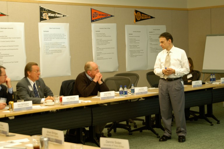 People sit around a table with college flags on the wall for Kauffman Campuses.