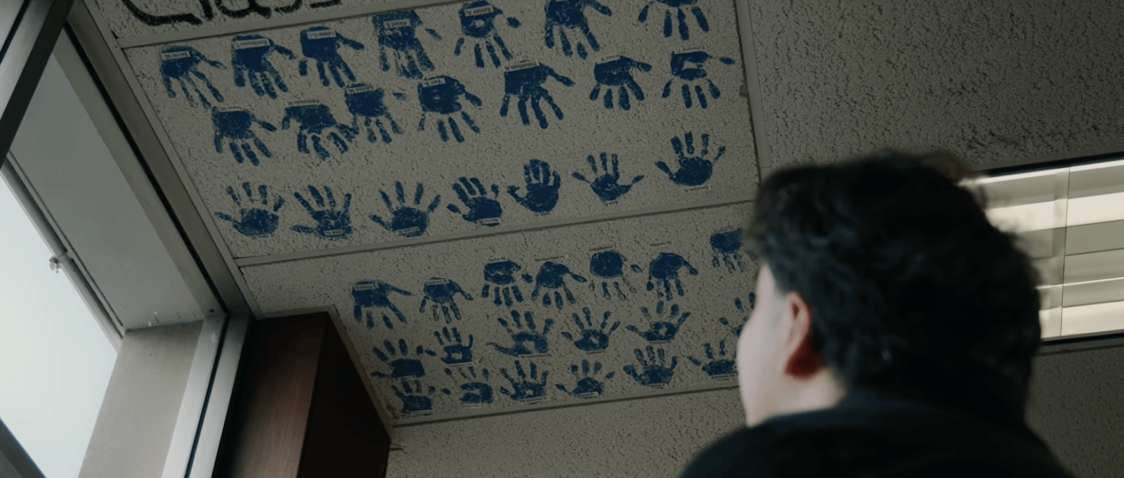 A person looks up to the ceiling covered in a series of handprints made out of blue paint.